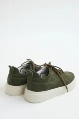 Zapatillas de gamuza color verde oliva con cordones marrones, pespuntes decorativos y suela de plataforma blanca.