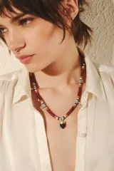 Collar corto de cuentas chatas multicolor con arandelas doradas y dijes de strass plateados en forma de gota. Dije central de piedra negra con engarce dorado. Cierre con gancho y cadena de extensión.