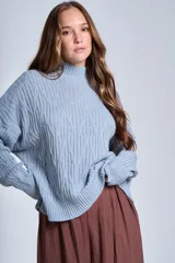 Sweater color crema de punto trenzado, con cuello alto y mangas largas.