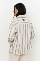 Chaqueta de algodón a rayas verticales en tonos beige y gris, con cuello camisero, cierre frontal con botones y mangas largas con puños abotonados. Tiene bolsillos delanteros con solapa y galones ondeados a tono.