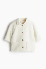 Chaqueta corta color crema en tejido texturizado con cuello clásico y botones metálicos decorativos. De corte ajustado con mangas raglán al codo y bolsillos de parche delanteros. Forrada.