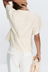 Camiseta color crudo de algodón con cuello redondo, manga corta caída y cintura ajustable con cordón.