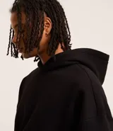 Buzo negro con capucha, manga larga, bolsillo canguro y barras ajustadas. Corte boxy.
