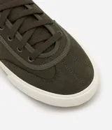 Championes casuales color verde militar, confeccionados en sarga con recortes laterales y ajuste con cordones. Suela de goma blanca con base marrón.