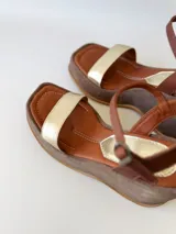 Sandalias de cuero con plataforma, color marrón con tira dorada sobre los dedos y tobillera marrón con hebilla.