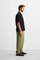 Pantalón verde oliva de corte relaxed fit, confeccionado en tejido de algodón con textura. Tiene cintura elástica ajustable con cordón, bolsillos frontales y un bolsillo trasero de parche.