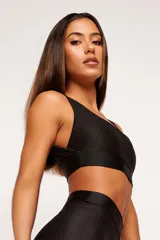 Top deportivo negro con textura colmena 3D, escote cuadrado, breteles anchos y banda inferior con logo.