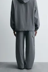 Pantalón cargo gris con textura acanalada, corte relaxed fit, cintura elástica con pliegues frontales, bolsillos laterales tipo cargo con solapa, bolsillos frontales y traseros de vivo, cierre frontal con cremallera y botón.