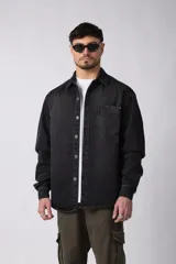 Chaqueta de jean negro desgastado, de corte recto, con cuello clásico, cierre frontal con botones y bolsillo en el pecho. Confeccionada en denim de algodón de 12 onzas.