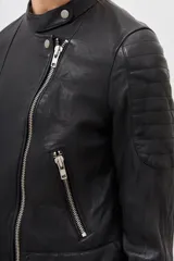 Campera negra de cuero ovino con efecto arrugado. Tiene cuello mao, cierre metálico frontal, bolsillos con cierre, puños con cierre y snaps metálicos. Detalles de matelaseado en hombros y cintura.