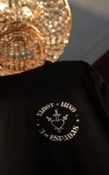 Remera negra de algodón con cuello redondo y calce oversize. Estampa frontal con diseño de tarot con un corazón atravesado por tres espadas y la frase "3 de Espadas".