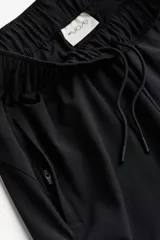 Pantalón de correr negro de tejido funcional DryMove™, corte estándar, cintura elástica con cordón, bolsillos laterales con cierre oculto, piernas levemente ajustadas con elástico revestido y cierre en los bajos. Stretch en cuatro direcciones.