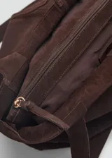 Bolso shopper de gamuza marrón chocolate, con doble asa corta y asa de hombro. Tiene cierre de cremallera y lazo ajustable.