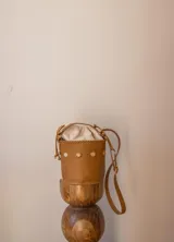 Cartera tipo canasta color terracota con textura símil piel de cocodrilo, con forro de tela blanca ajustable con cordón. Tiene correa larga de cuero marrón con hebilla dorada.