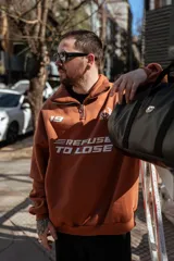 Buzo marrón con cierre medio, cuello alto y corte oversize. Estampado frontal con el número 19, un ancla con laureles y la frase "Refuse to Lose".