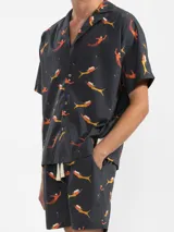 Camisa de manga corta con cuello estilo camper y estampado de sirenas en tonos naranja y amarillo. Tiene botones de madera y parche con logo. Corte boxy.