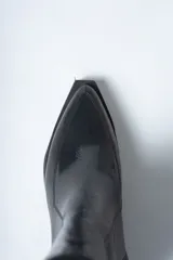 Bota corta negra de cuero con caña ajustada, punta cuadrada y taco ancho y bajo. Presenta un cierre lateral y costuras visibles en el empeine.