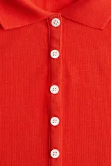 Remera polo roja de punto acanalado, corte entallado, con cuello clásico, tapeta de botones y mangas cortas.