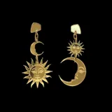 Aros de metal dorado que presentan un diseño de sol y luna, simbolizando la dualidad.