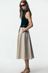 Vestido midi con falda beige con botones y cuerpo negro de cuello alto y sin mangas. Incluye cinturón negro con hebilla plateada.