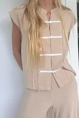 Blusa color beige confeccionada en lino tusor, de corte recto, con cuello mao y cierre frontal con botones forrados. Presenta mangas cortas y ruedo con terminación desflecada.