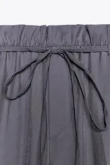 Pantalón gris de tejido fluido, tiro alto con cintura tipo paper bag, bolsillos laterales y cinturón lazada en el mismo tejido.