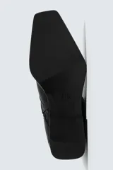 Botín de cuero negro con punta cuadrada, caña corta y cierre lateral con cremallera. Presenta una correa con hebilla metálica alrededor del tobillo.