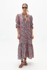 Vestido midi de lino color ladrillo con estampado floral celeste, corte recto, cuello mao, mangas abullonadas 3/4 con puños elásticos, cierre frontal con botones y falda con volantes.