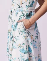 Vestido midi blanco con estampado floral celeste y verde, escote recto con tirantes, abertura frontal con botones, lazo en la cintura y bolsillos laterales.
