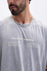 Remera de manga corta, corte oversize, color gris con efecto lavado (acid wash). Presenta un estampado minimalista en el pecho con texto que incluye "VILLA CLUB / SEASON 01".