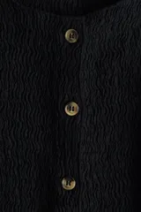Chaleco negro entallado de punto texturizado con cuello redondo y botones frontales.