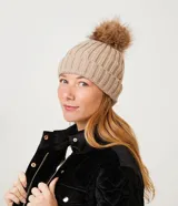 Gorro de punto acanalado color beige, con pompón marrón y borde inferior doblado.