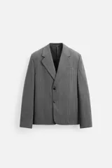 Blazer gris con raya diplomática, corte boxy, cuello con solapas de muesca, manga larga con puño abotonado, bolsillo de vivo en pecho, aberturas en espalda y cierre frontal con dos botones.