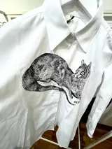 Camisa blanca de algodón con cuello clásico, manga larga con puños abotonados y estampado frontal de un animal similar a un zorro.