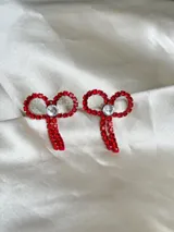 Par de aros colgantes con forma de moño, confeccionados con strass rojos y un cristal central.
