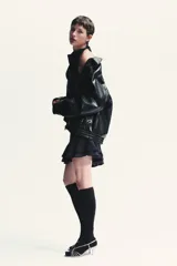 Chaqueta bomber negra de efecto piel, con cuello solapa y manga larga acabada en puño con botón. Tiene bolsillos de vivo en el delantero, bajo con elástico y cierre frontal con cremallera metálica y solapa con botones.