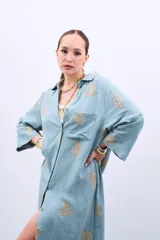 Vestido camisero largo celeste con bordado dorado de hojas, corte holgado, manga larga y cierre frontal con botones.