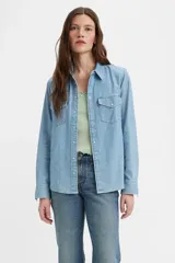 Camisa de denim celeste de manga larga con cuello clásico, cierre frontal con botones a presión, dos bolsillos en el pecho con solapa abotonada y corte recto.