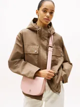 Cartera saddle Tommy Hilfiger color rosa con correa de textil trenzado con inscripciones de la marca y logo TH brillante en el frente.