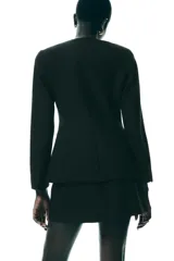 Blazer negra entallada, de escote pico y manga larga con hombreras. Tiene bolsillos delanteros de vivo y cierre frontal con botones a presión ocultos.