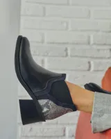 Bota corta de cuero sintético negro con elástico lateral y detalle de estampado animal print en el talón.