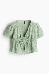 Top corto verde agua en punto arrugado con escote en V y doble cordón de ajuste abajo del busto que se enlaza adelante. Mangas cortas con elástico revestido y ribete sobrehilado.