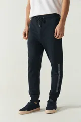 Pantalón de jogging negro de felpa con puños y cintura ajustable con cordón. Presenta logo de goma en la pierna izquierda y bolsillos laterales.