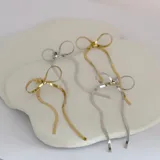 Par de aros colgantes dorados con forma de moño, confeccionados en acero quirúrgico hipoalergénico con baño de oro de 18K.