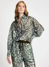 Camisa de manga larga con estampado animal print en tonos verde, marrón y blanco. Tiene cuello clásico, cierre frontal con botones y puños con tres botones.