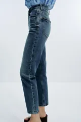 Pantalón de jean azul de tiro alto, corte mom fit, tobillero y con cinco bolsillos. Cierre frontal con cremallera y botón.