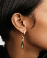 Aro individual dorado con forma de argolla y dije colgante en forma de gota.