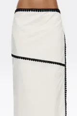 Falda pareo midi color blanco con bodoques negros a contraste y cierre con lazo en la cintura.
