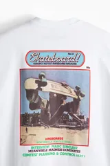 Remera blanca de algodón pesado con cuello redondo ribeteado, hombros caídos, bajo recto y estampado pequeño en el pecho. Corte oversized.