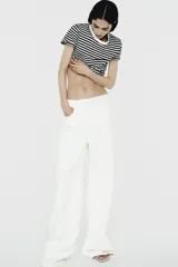 Pantalón de jean blanco de tiro alto, corte wide leg y relaxed fit. Con trabillas en la cintura, bolsillos delanteros y traseros, raya planchada en el frente y cierre frontal con cremallera, botón interior y gancho metálico.
